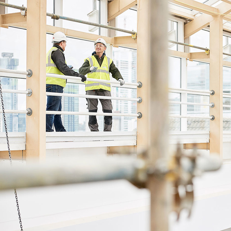 Two men in safety vests standing on a balcony overlooking a construction site.